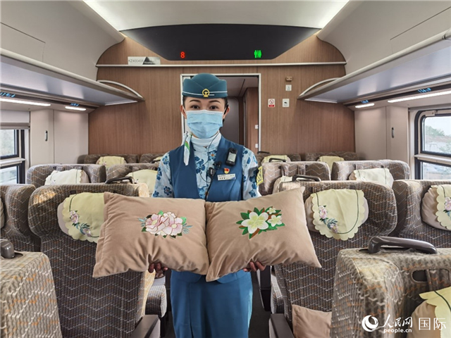 趙瑩靜展示中老鐵路國(guó)際旅客列車?yán)飵в兄袊?guó)牡丹花和老撾占巴花刺繡圖案的靠墊。人民網(wǎng)記者 杜明明攝