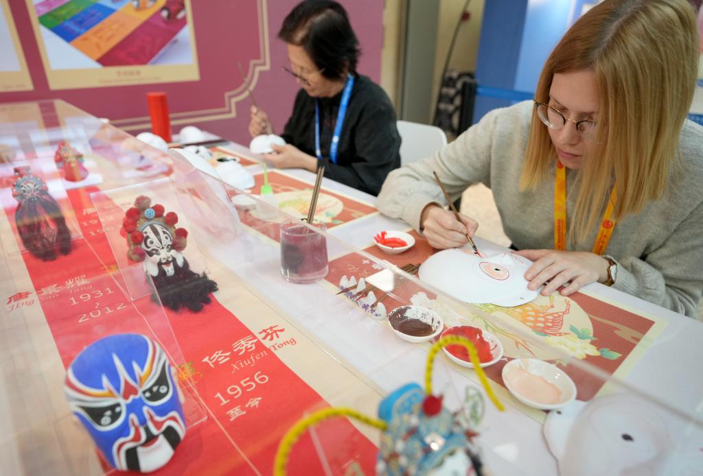 10月16日，在第三屆“一帶一路”國際合作高峰論壇新聞中心，來自比利時(shí)的記者（右）體驗(yàn)畫京劇臉譜。新華社記者 王毓國 攝