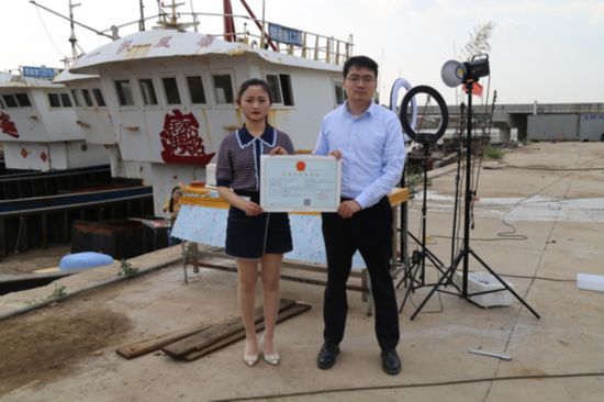 海鮮電商張夢琴與幫辦員手持食品經(jīng)營許可證合影。贛榆區(qū)委宣傳部供圖