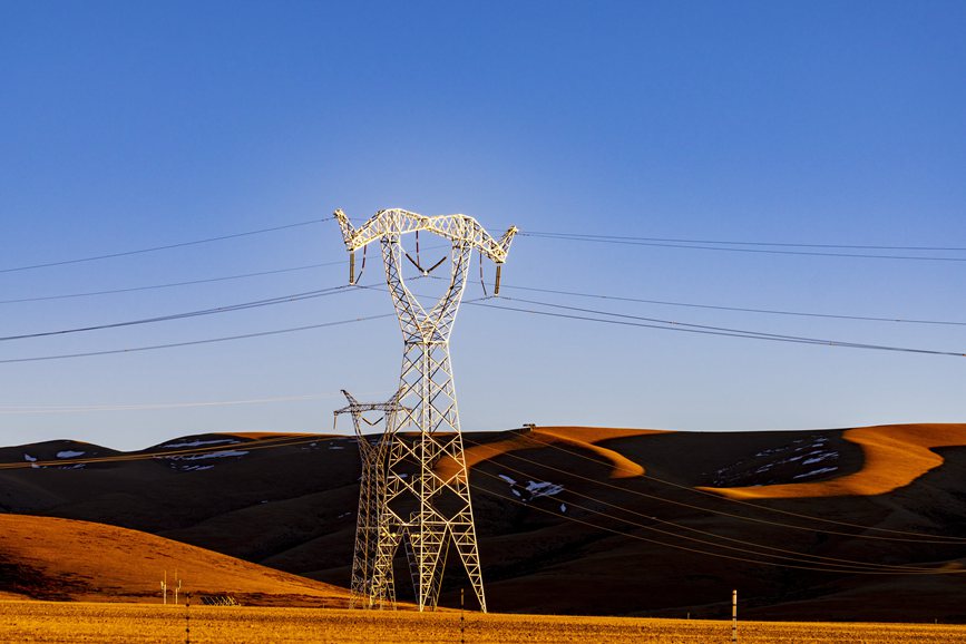 阿里地區(qū)的曠野上，電力鐵塔在夕陽下熠熠生輝。